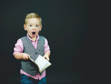 Kind mit Buch in der Hand reißt überrascht den Mund auf